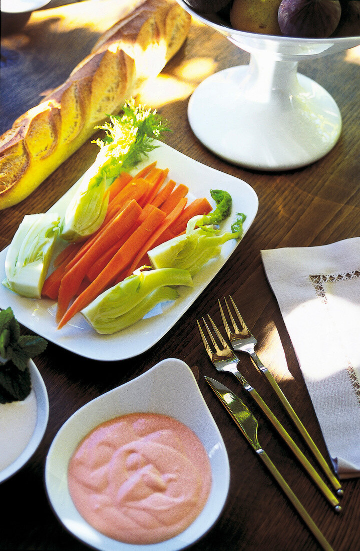 Baguette, frisches Gemüse und Dip auf Kastanienholztisch.