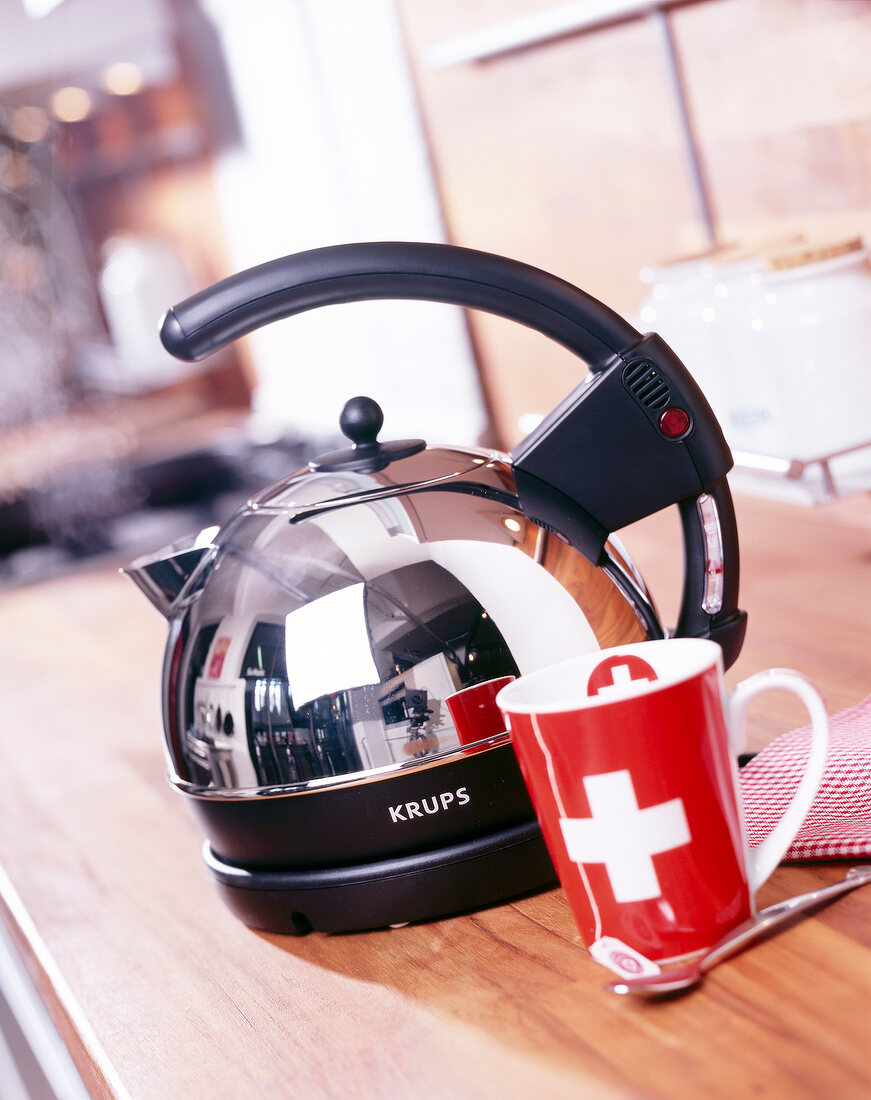 Kettle with black handle beside red cup on wooden table