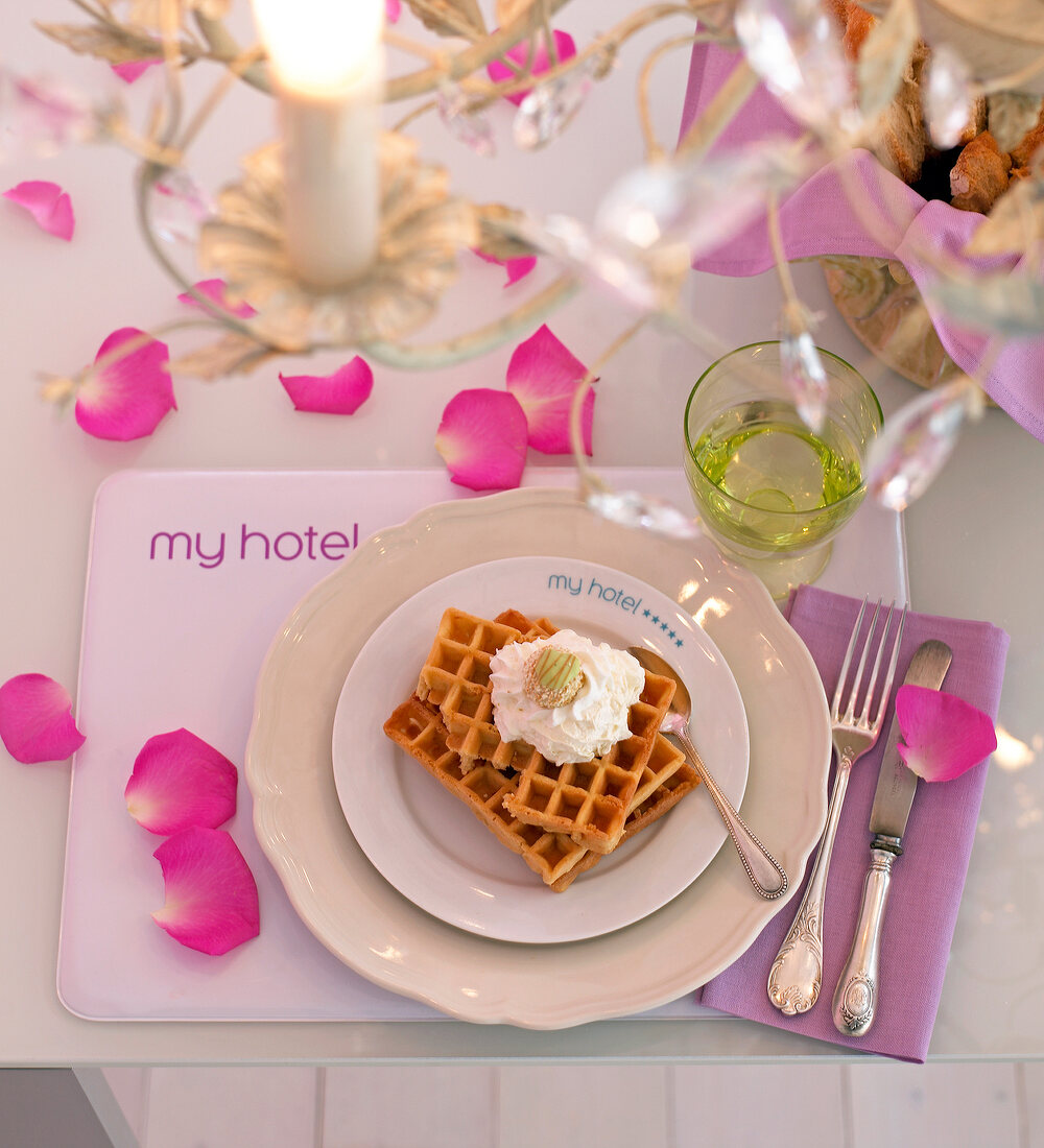 Waffles with white cream on plate decorated with rose petals on table