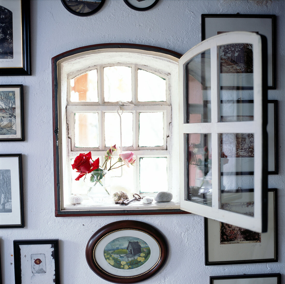 Kleines Fenster in einer weißen mit Bildern behangenen Wand.