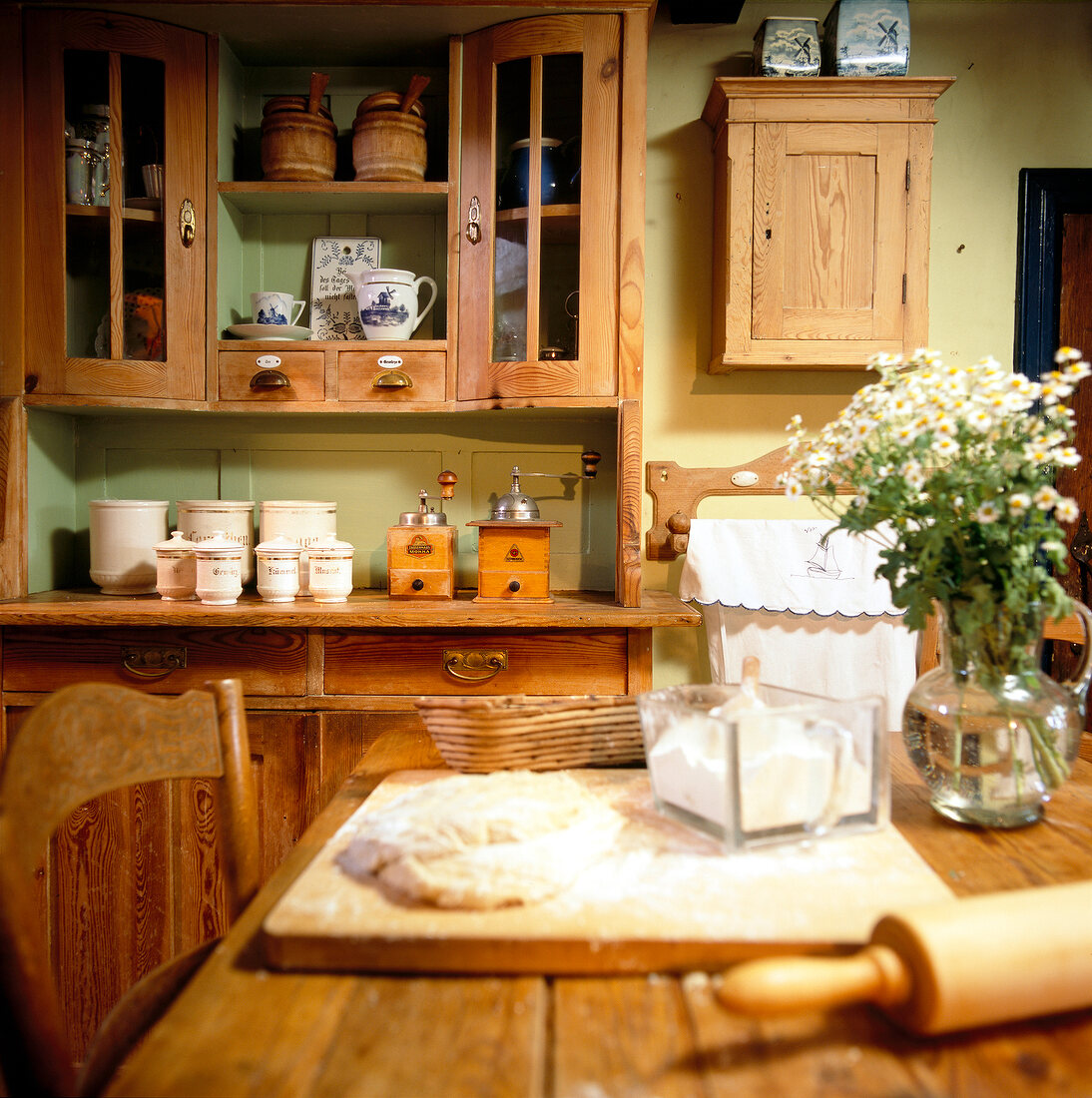 Dough and rolling pin on table in front of antique kitchen cabinet