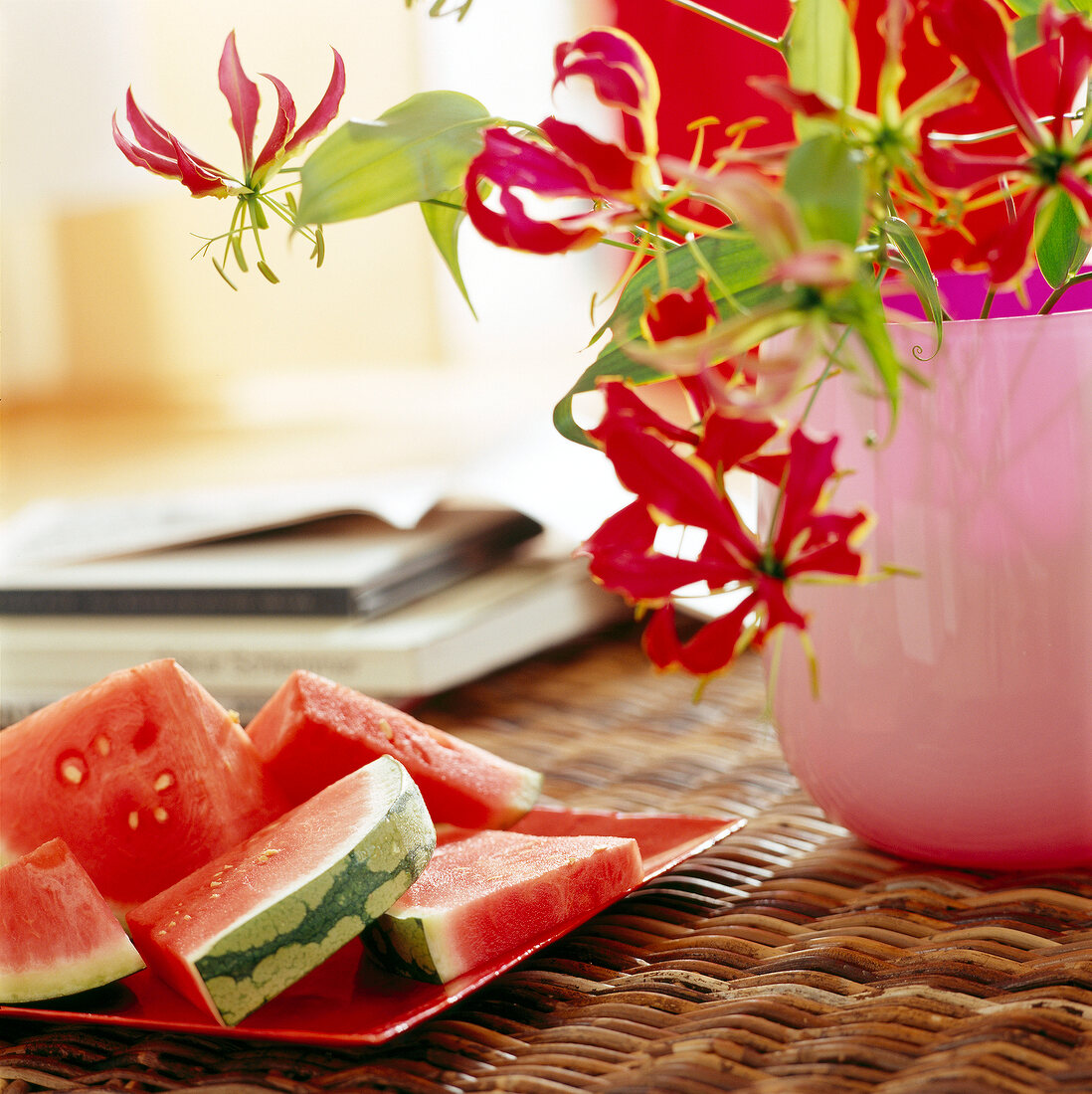 Melonenstücke auf einem Teller neben einer Blume auf einem Rattantisch.