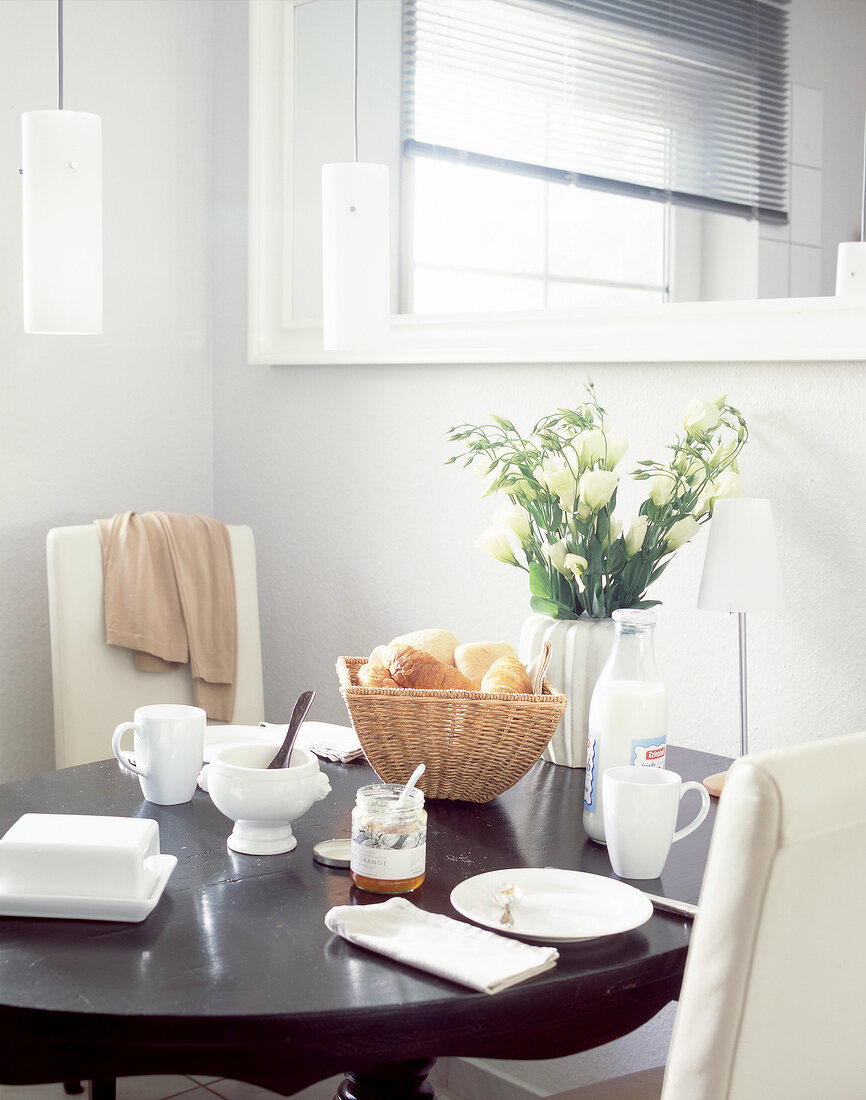 Black round wooden table laid for breakfast with flower vase