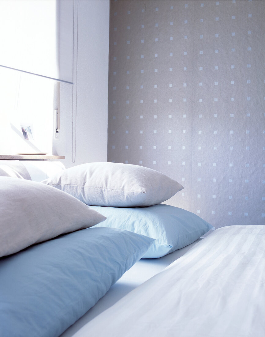 Close-up of blue and cream pillows on double bed against textile wallpaper