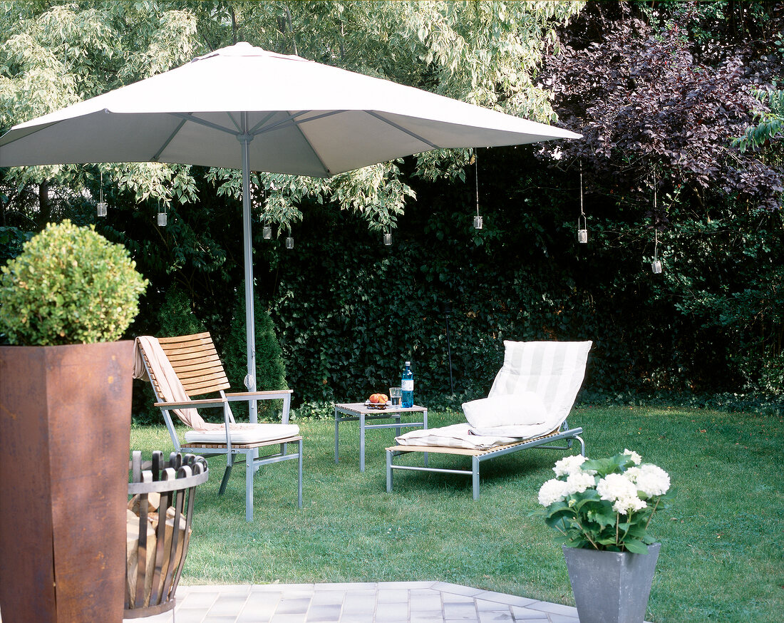Gartenliege und Gartenstuhl unter einem großen Sonnenschirm.