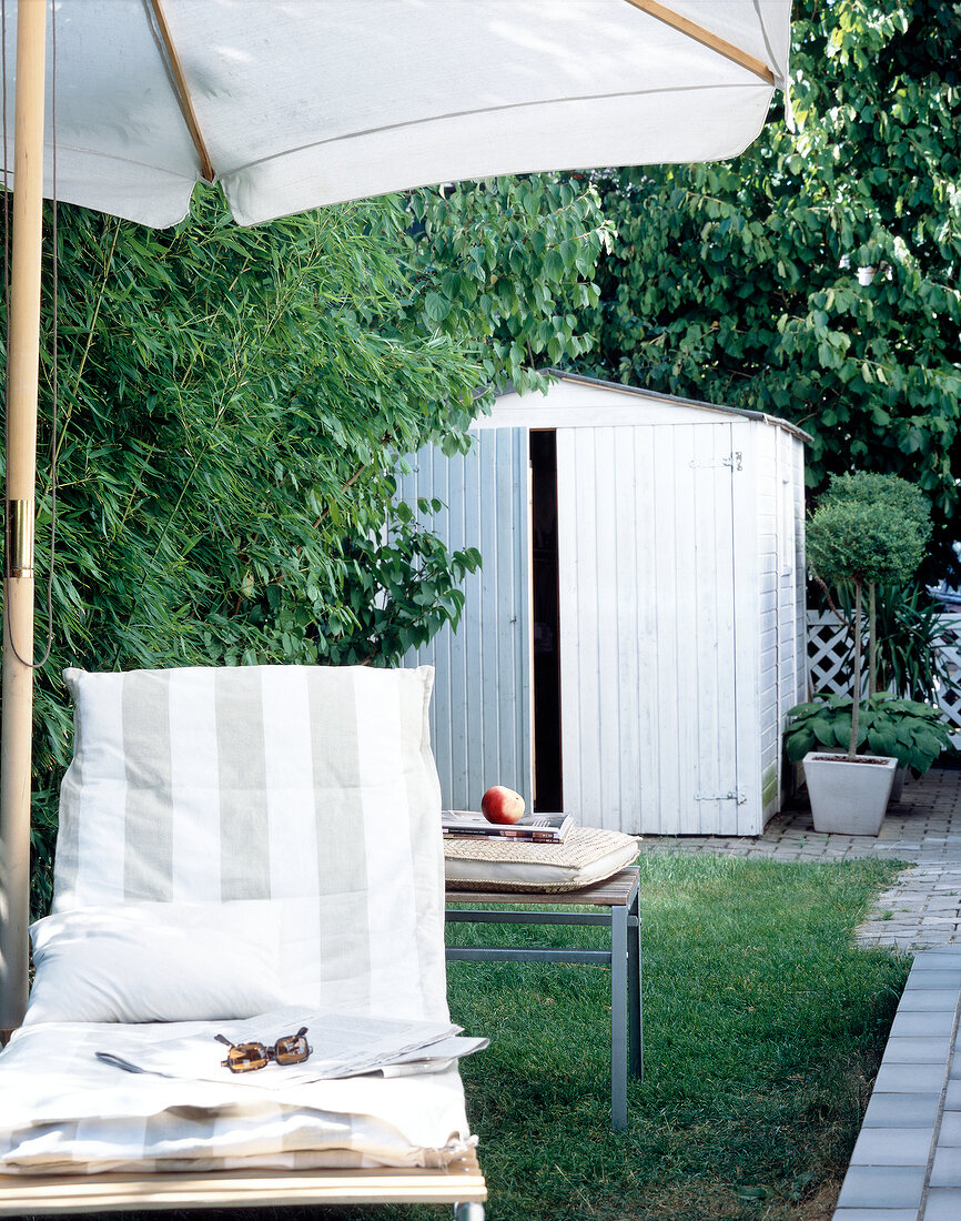 Close-up of lounger under a parasol against garden shed