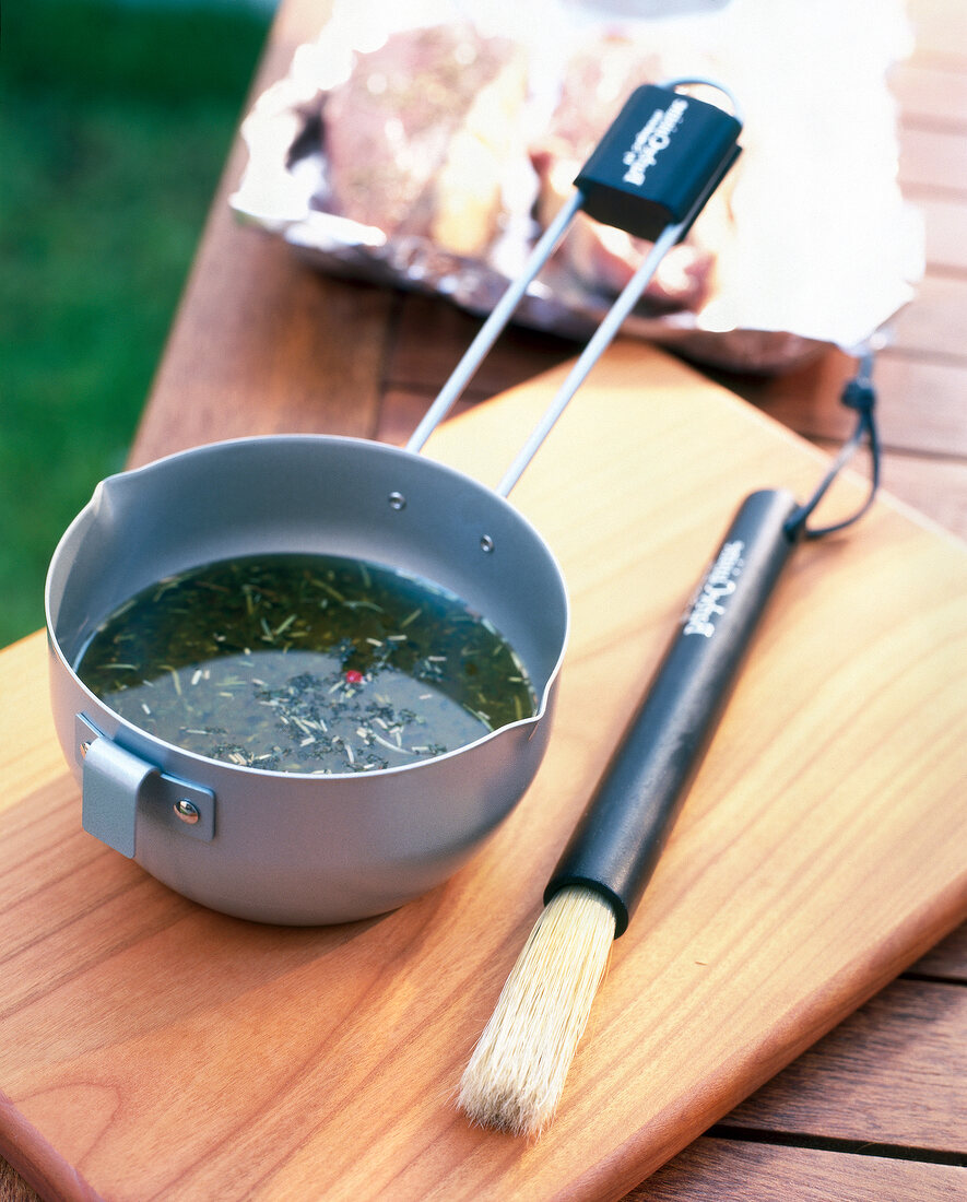 Saucepan with marinade and brush on wooden chopping board