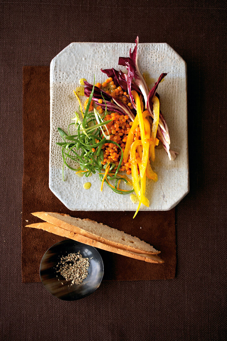 Salad with red lentils and slices of bread on square plate