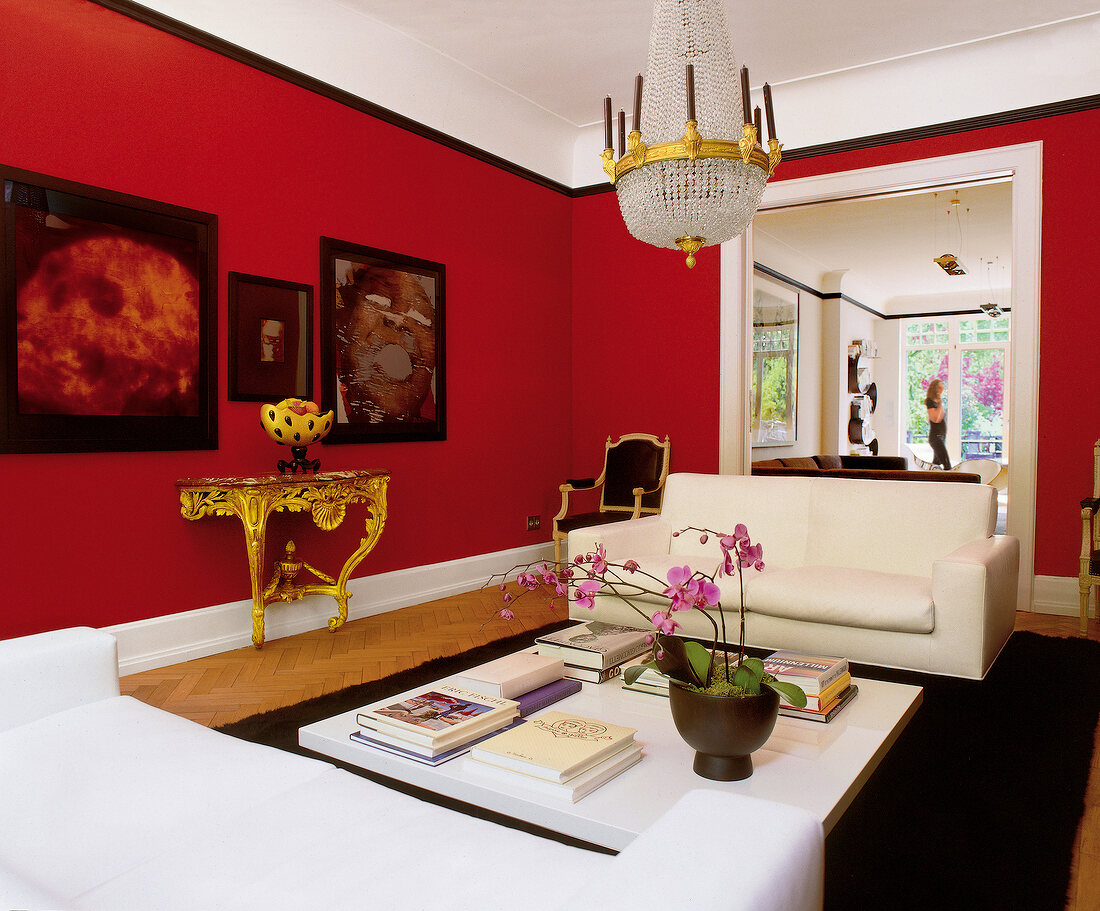 View of living room with red walls, white sofas and chandelier