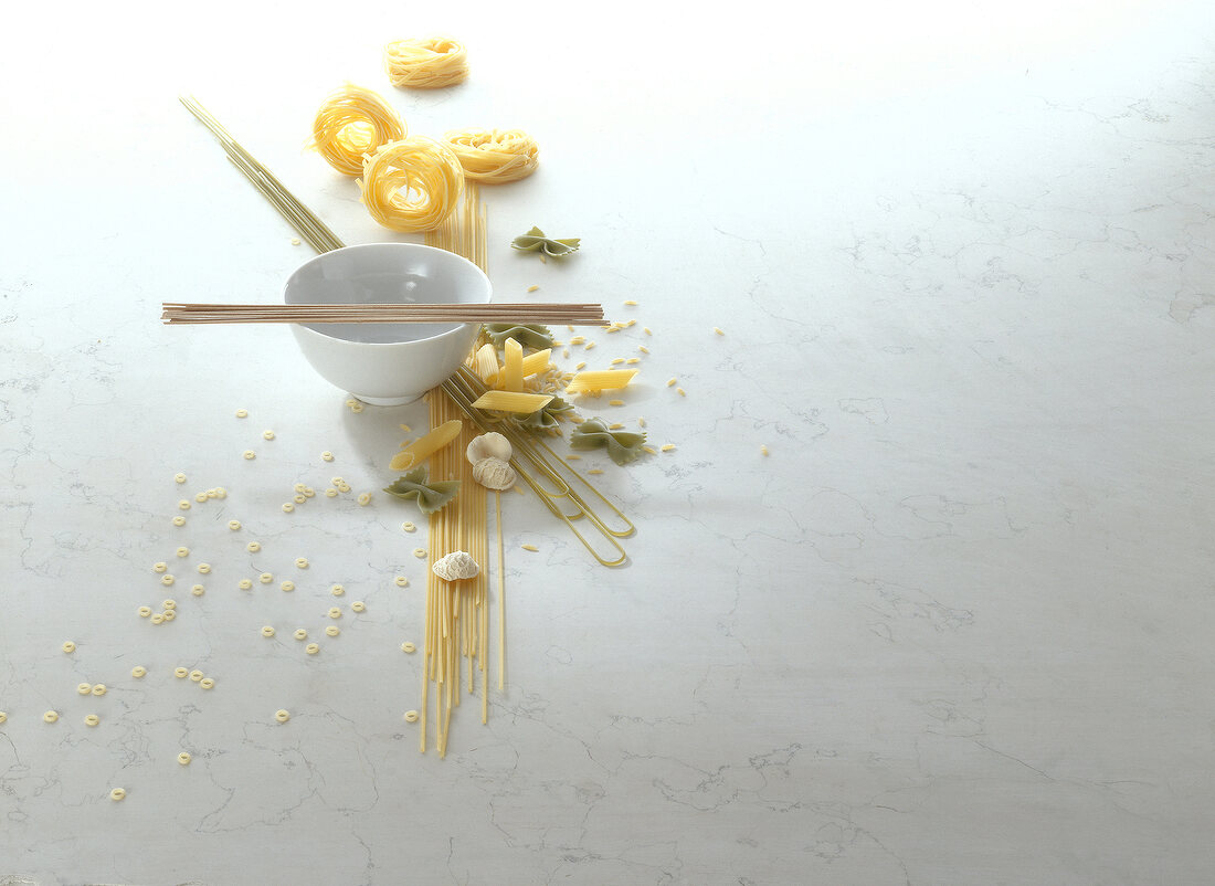 Bowl and different types of raw pasta on white background