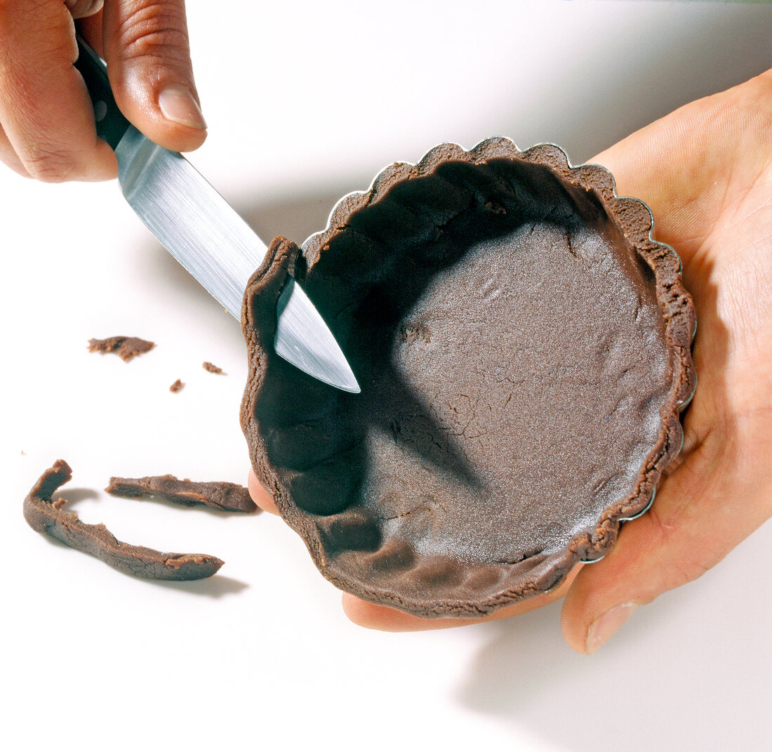 Close-up of hand cutting edges of chocolate dough in cake pan with knife