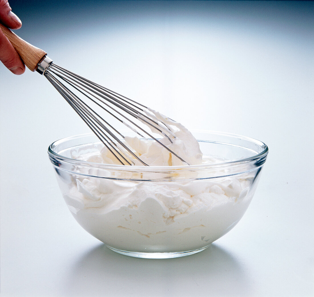 Cream being beaten with whisk in glass bowl