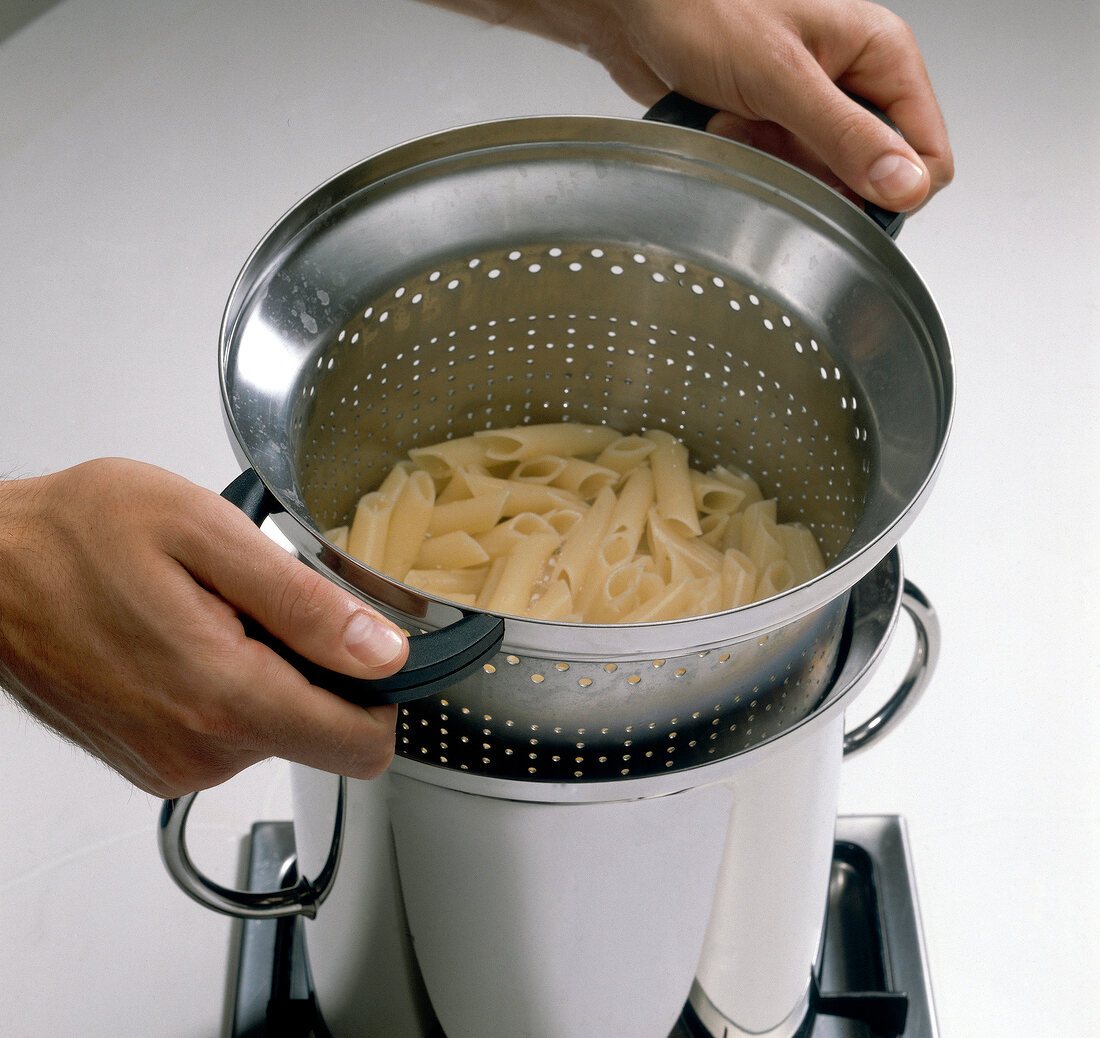 Hand draining boiled noodles in strainer for preparing pasta, step 3