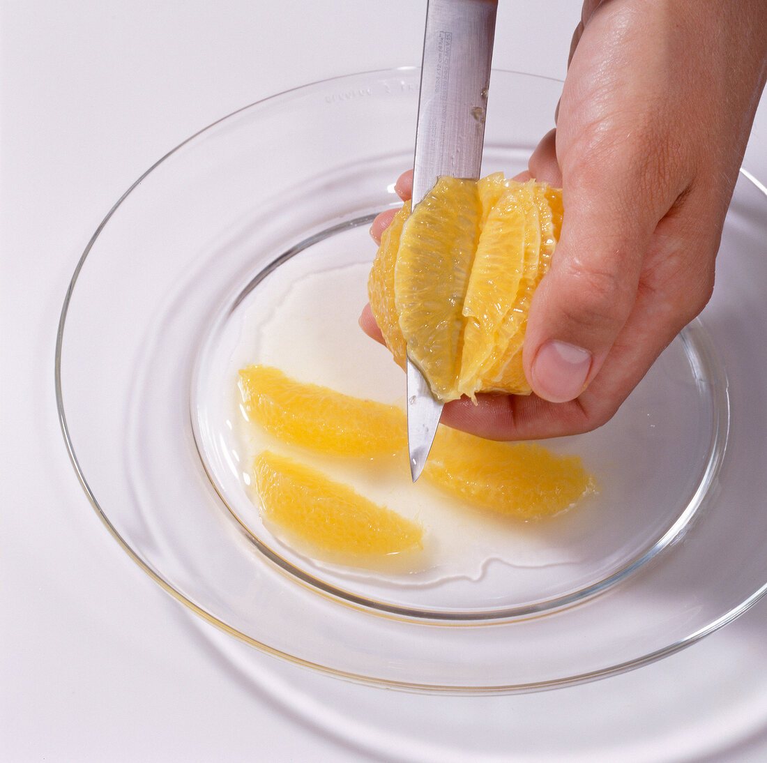 Hand slicing peeled orange with knife on glass plate