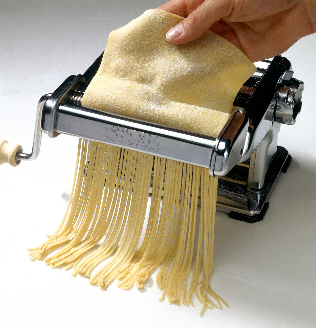 Taglierini pasta dough being cut into stripes in pasta machine