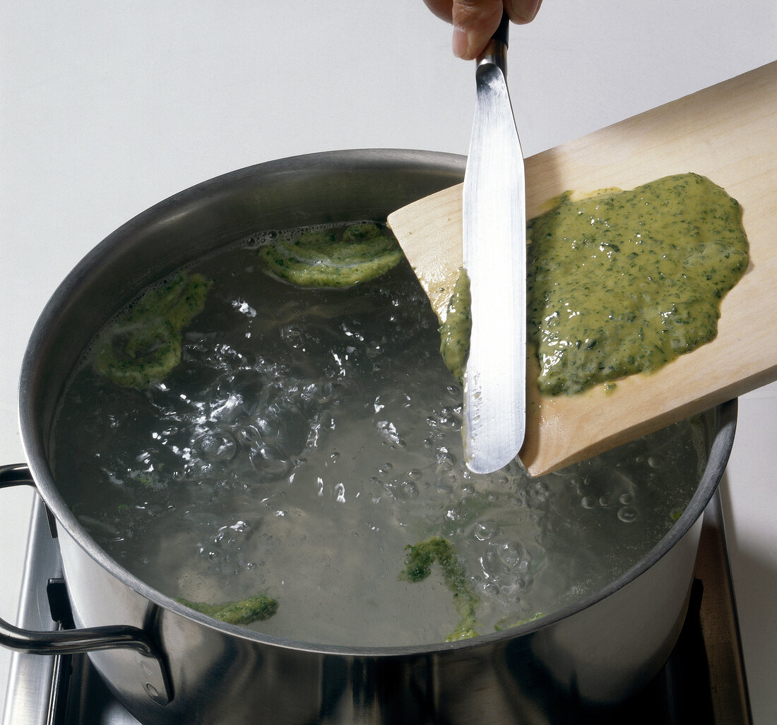 Herb spaetzle being added with spatula in boiling water, step 2