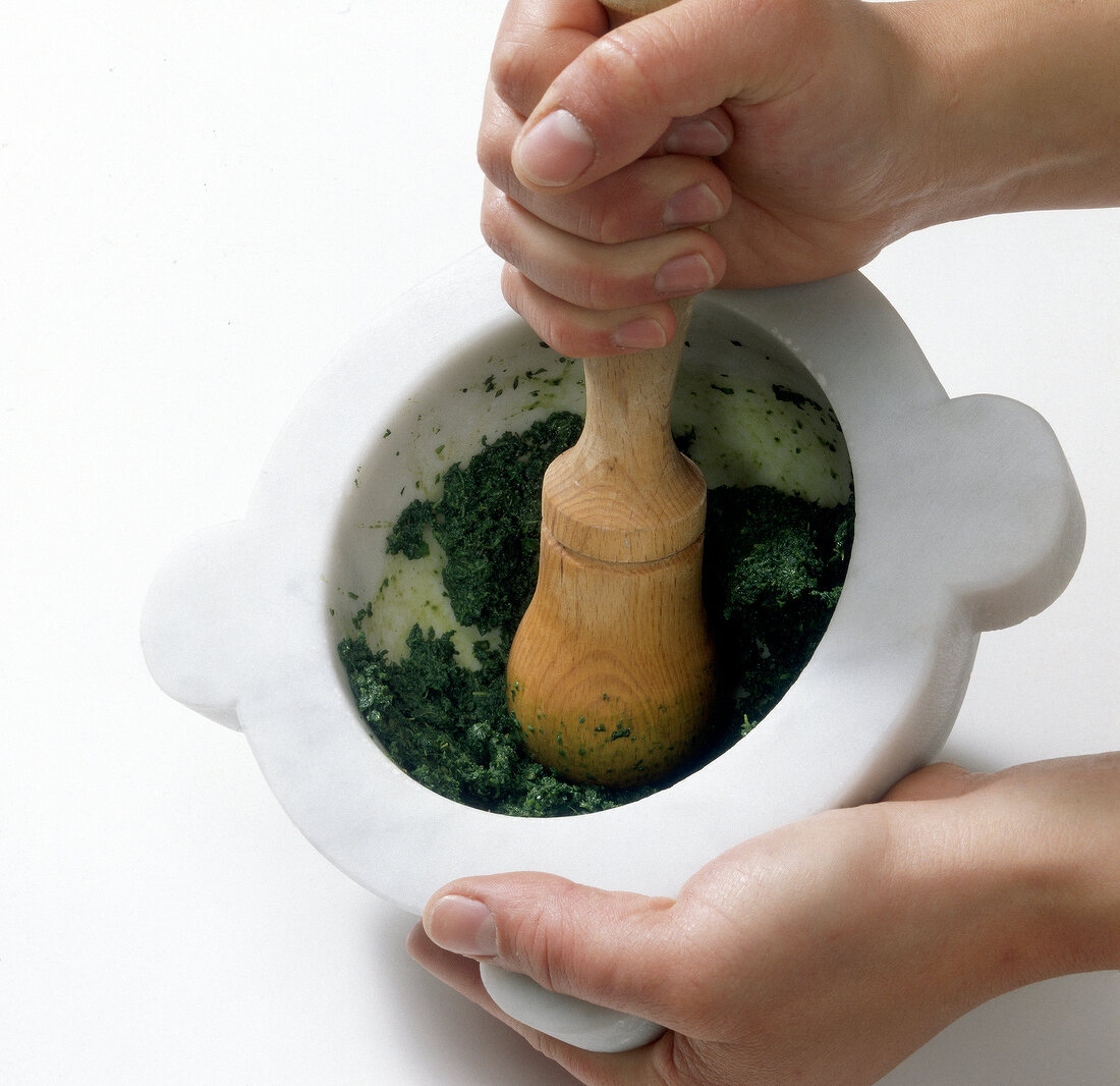 Basil leaves being mashed in mortar with pestle