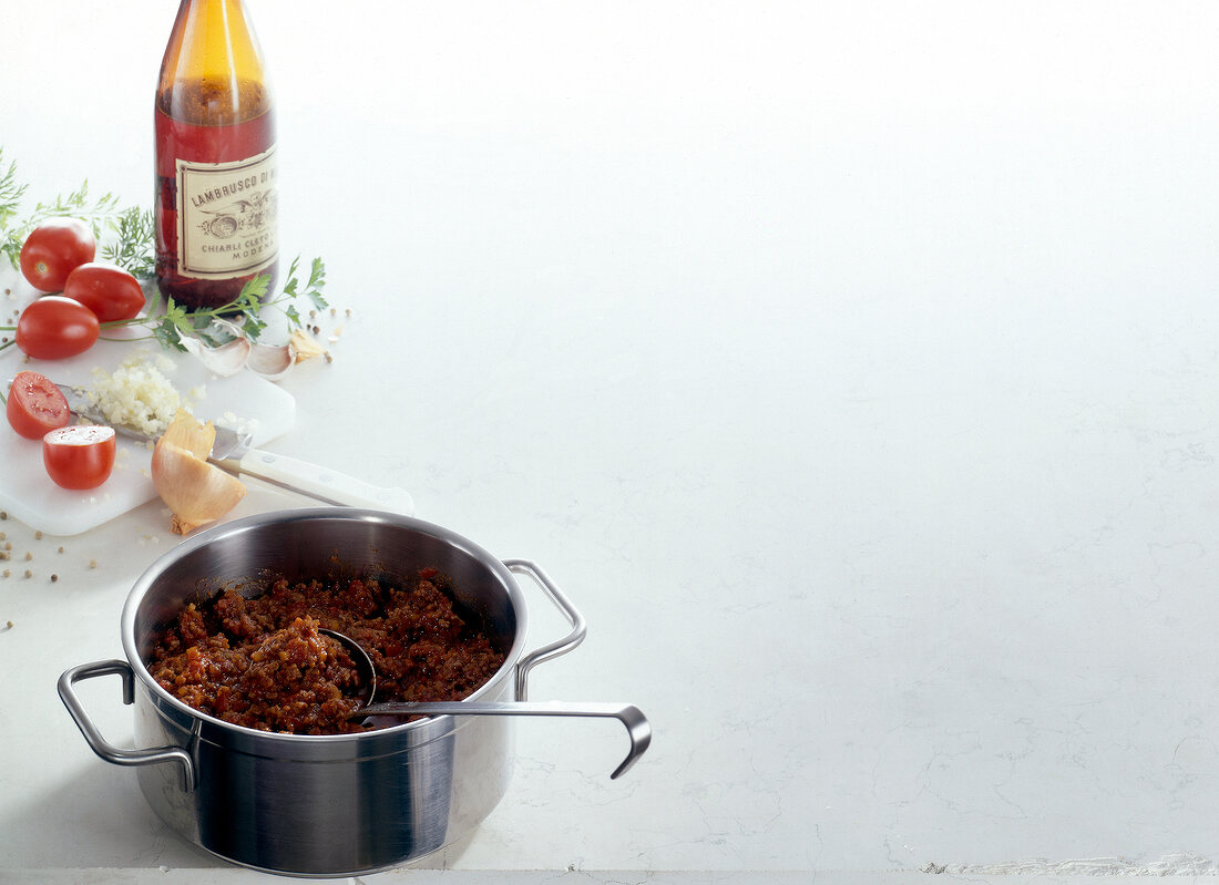 Rag alla bolognese in casserole with ingredients on white background, copy space