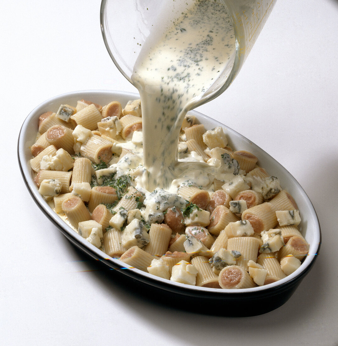 Cream being poured over stuffed pasta on tray, step 2