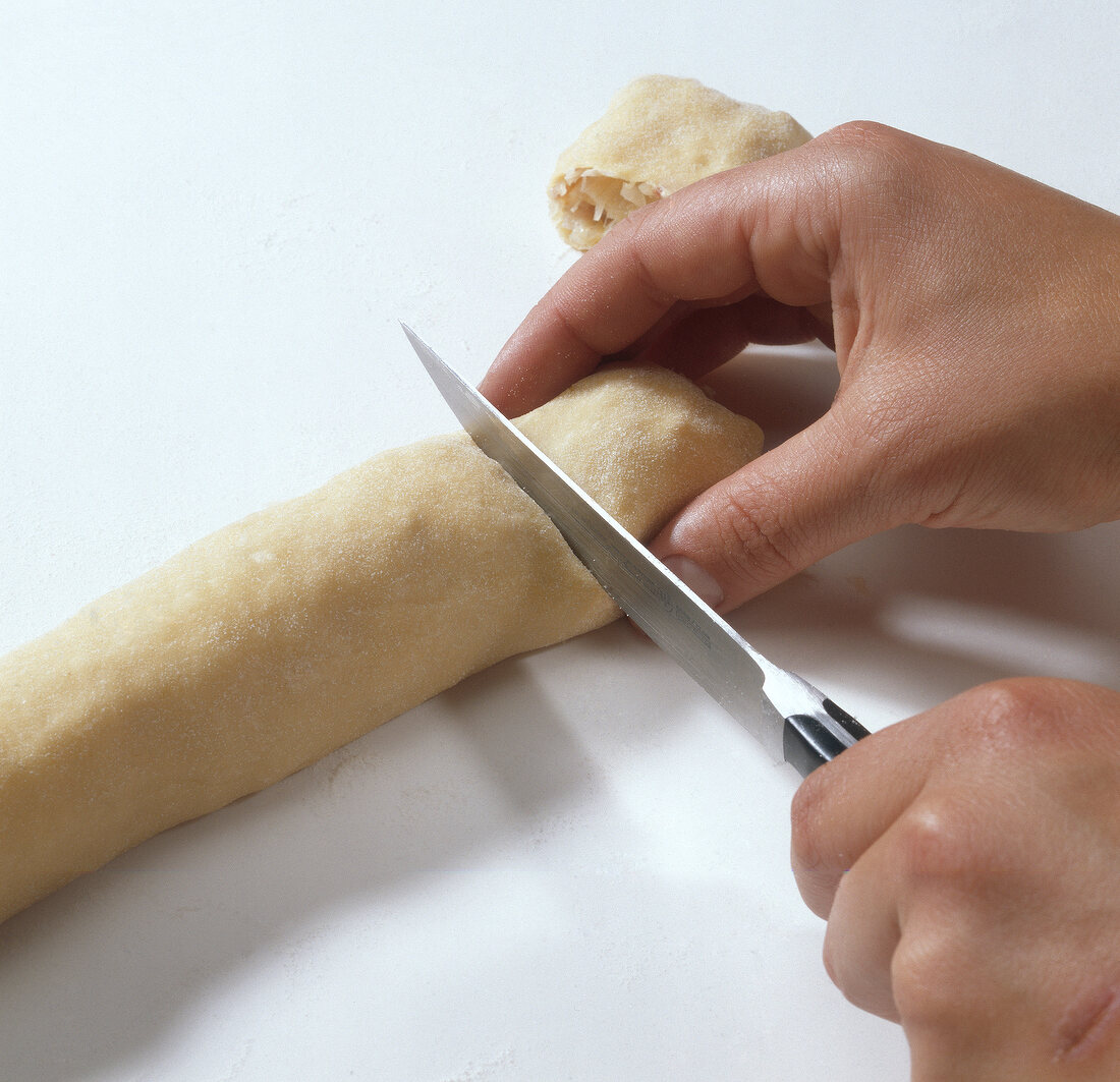 Hands cutting rolled dough with sauerkraut in pieces while preparing krautkrapfen, step 5