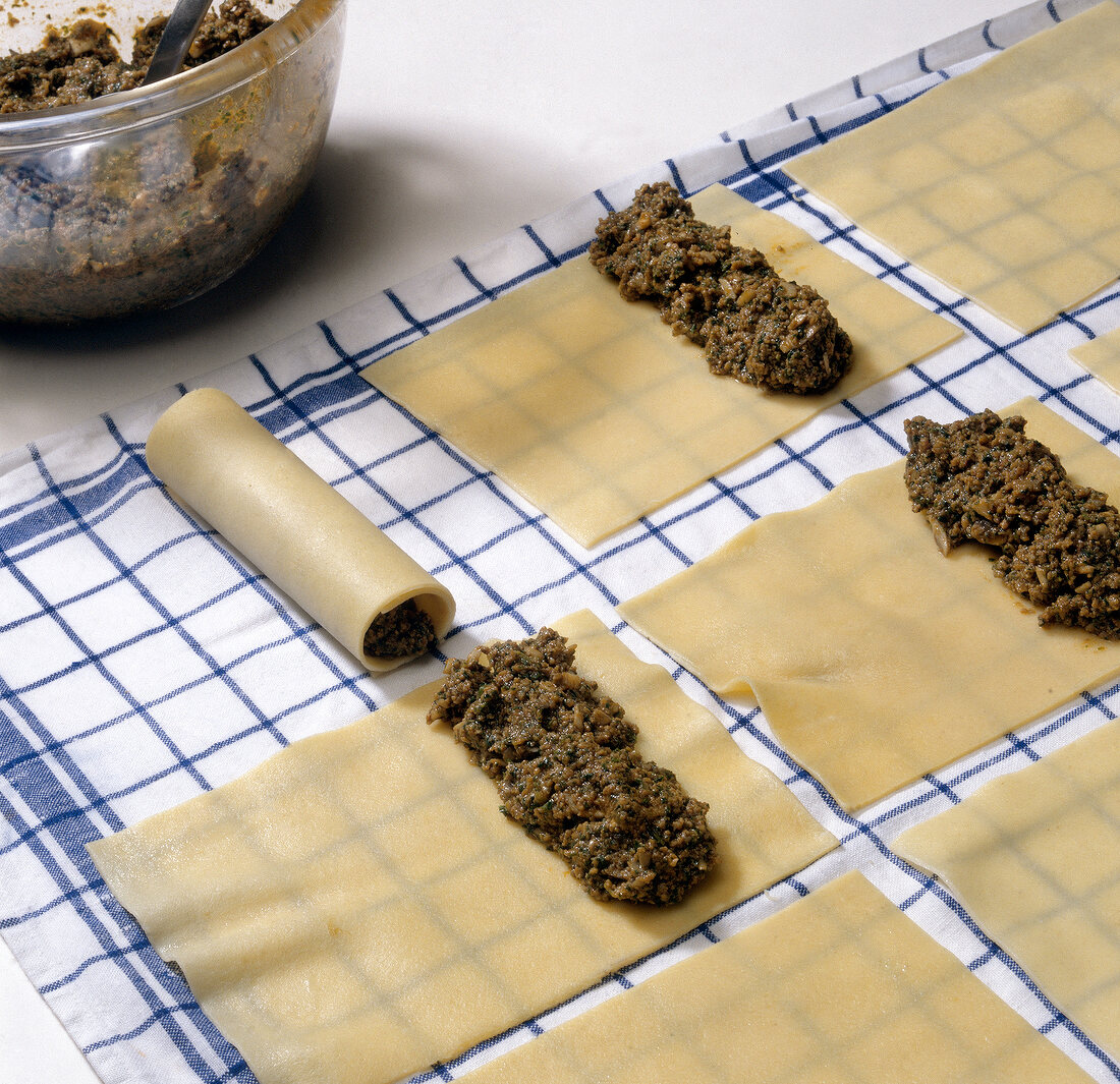 Pieces of pasta dough with filling being rolled while preparing cannelloni, step 1