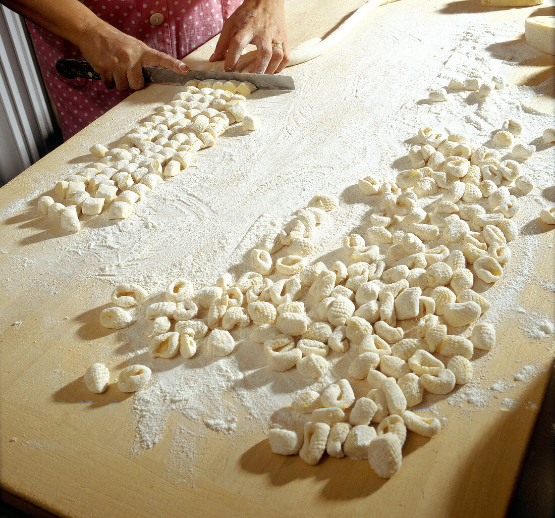 Woman's hands cutting rolled dough into pieces for preparation of gnocchi, step 3