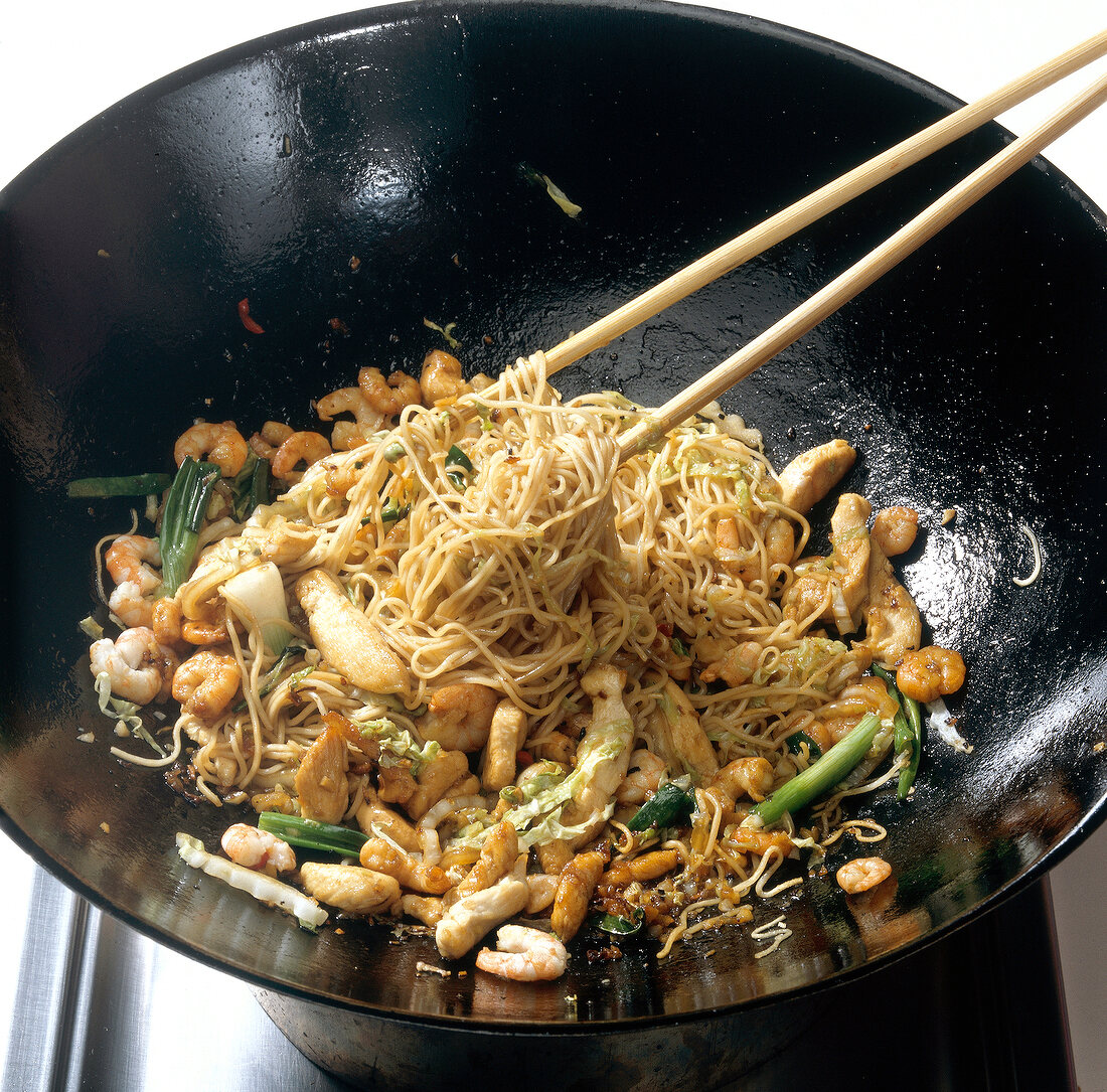 Boiled noodles and various ingredients in wok while preparing bami goreng pasta, step 6