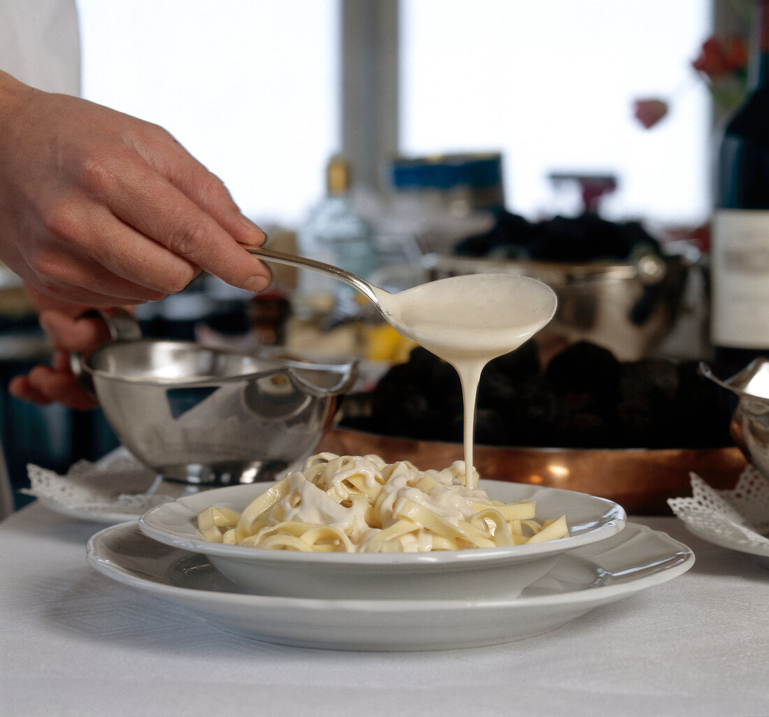 Cream sauce being poured over pasta while preparing tagliatelle alla mathis, step 1