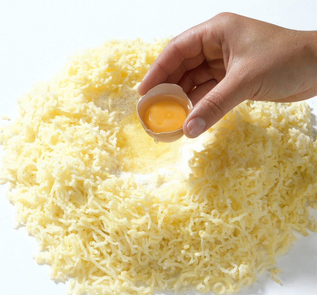 Egg being added to grated potatoes for preparing pasta, step 5