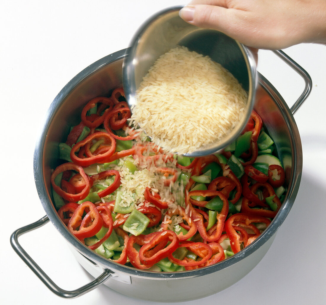 Rice being added to pot with vegetables and peppers, step 4