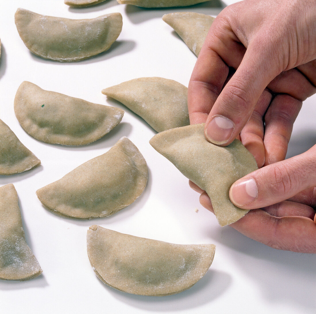 Stuffed dough slices in half moon shape being pressed on edges