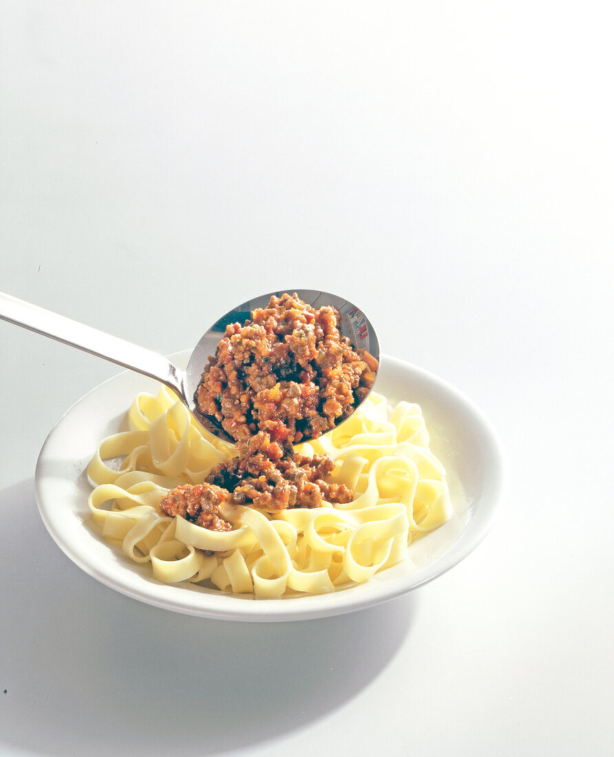 Plate of ribbon pasta with meat sauce on white background