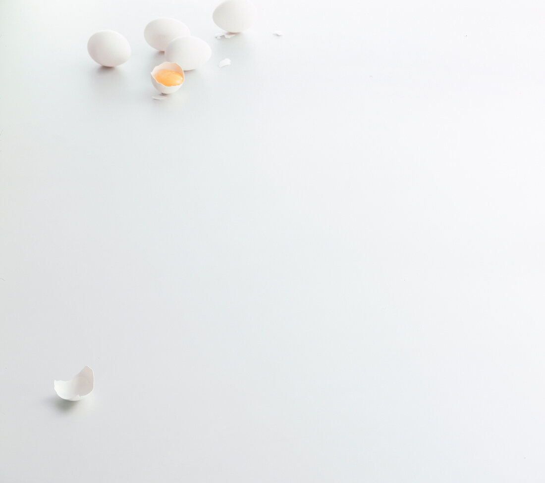 Four whole eggs and one halved egg on white background