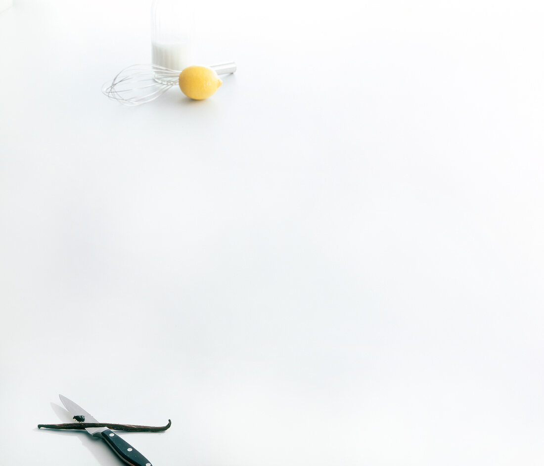 Glass of milk, lemon, whisk, vanilla bean and knife on white background, copy space