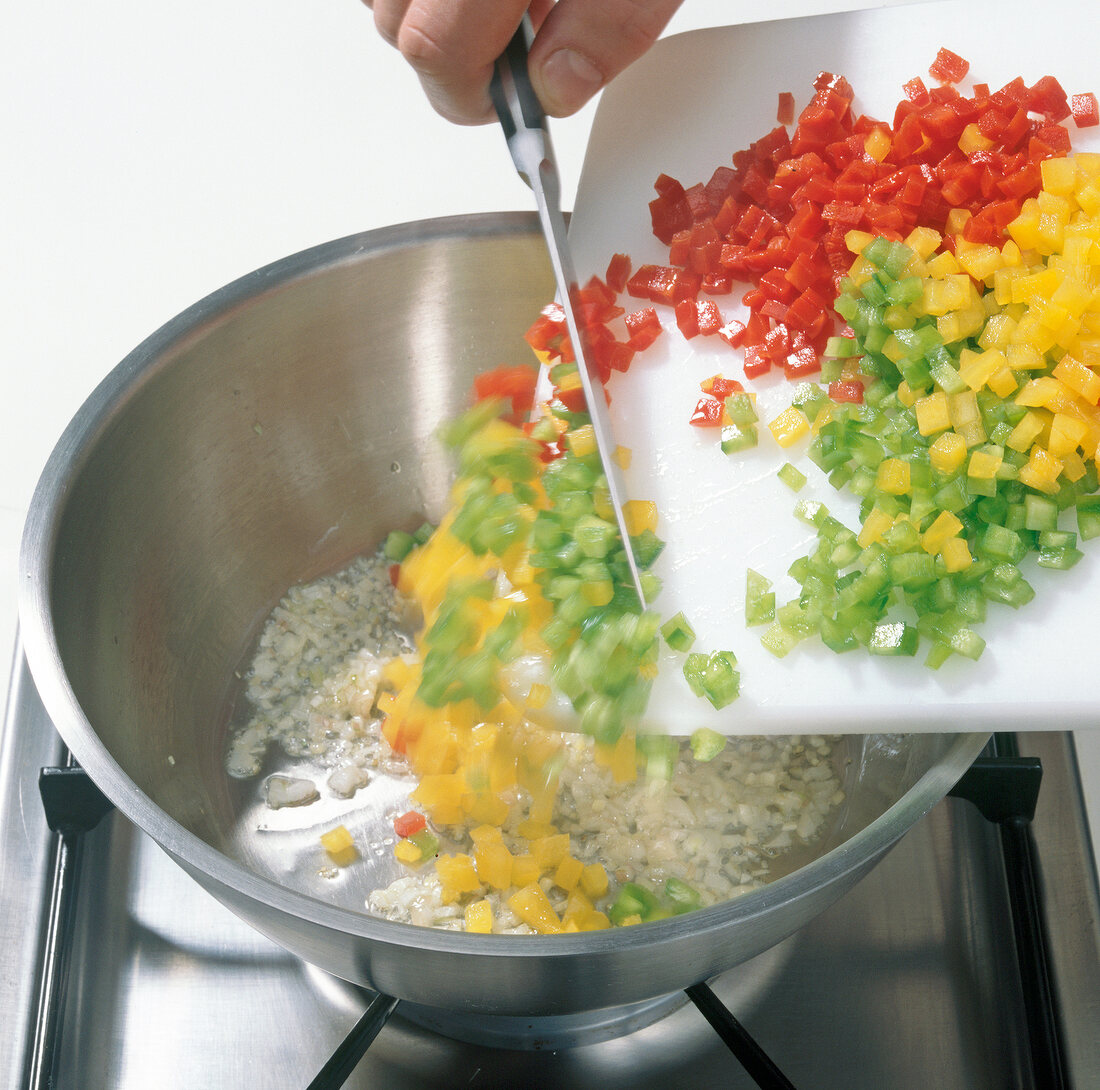 Yellow, green and red pepper cubes being added in pot for cooking