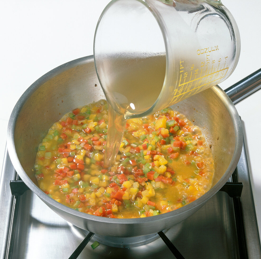 Stock being added to cook diced peppers in pot