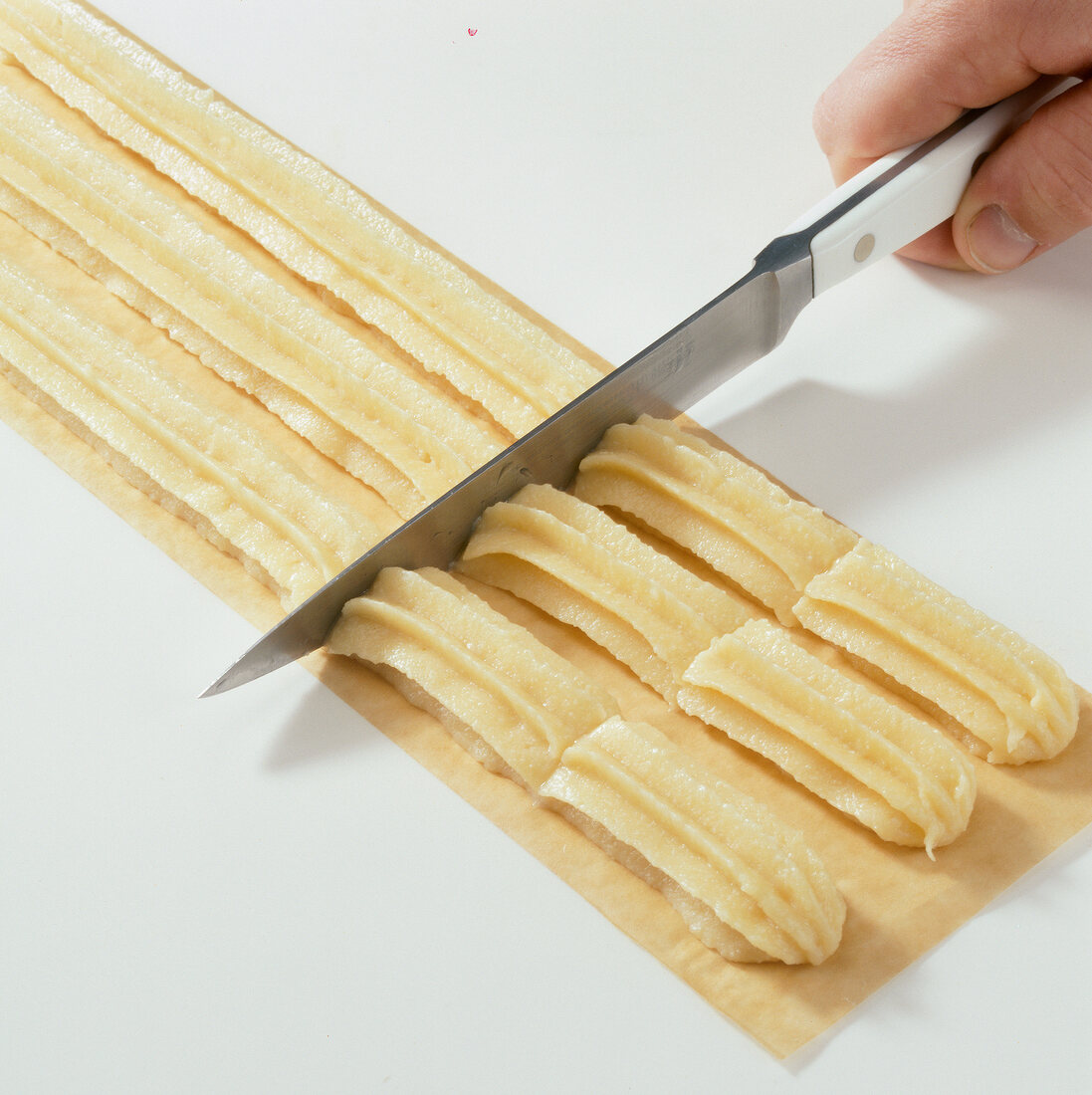 Pasta sheet topped with dough being cut into pieces