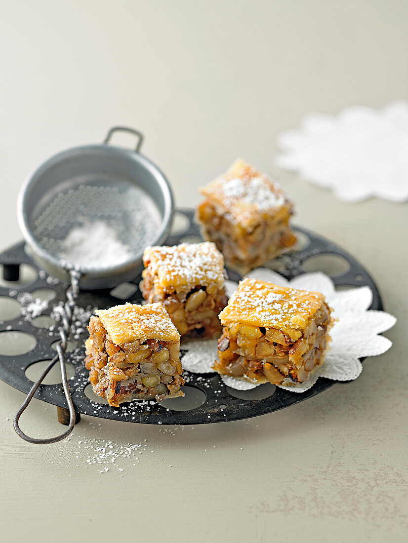 Pieces of nut baklava with icing sugar and strainer on plate