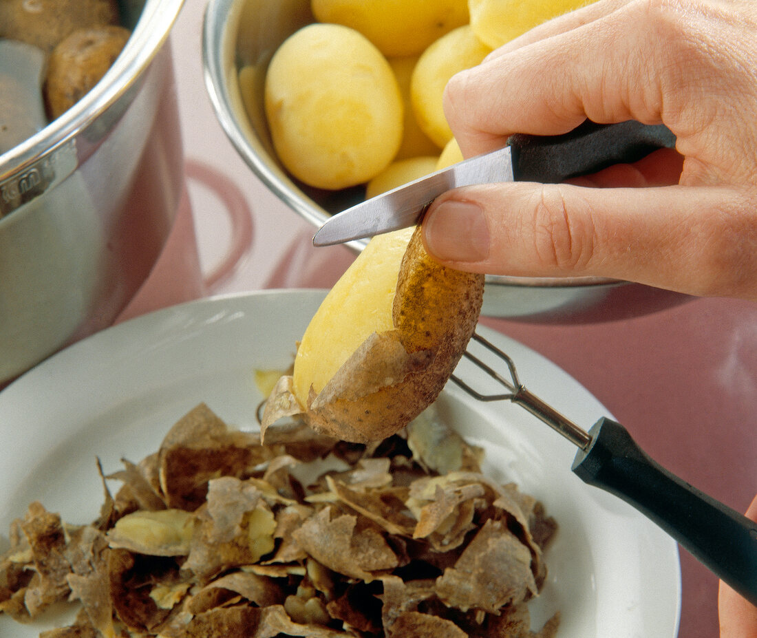 Hand being peeled boiled hot potatoes with knife and holder