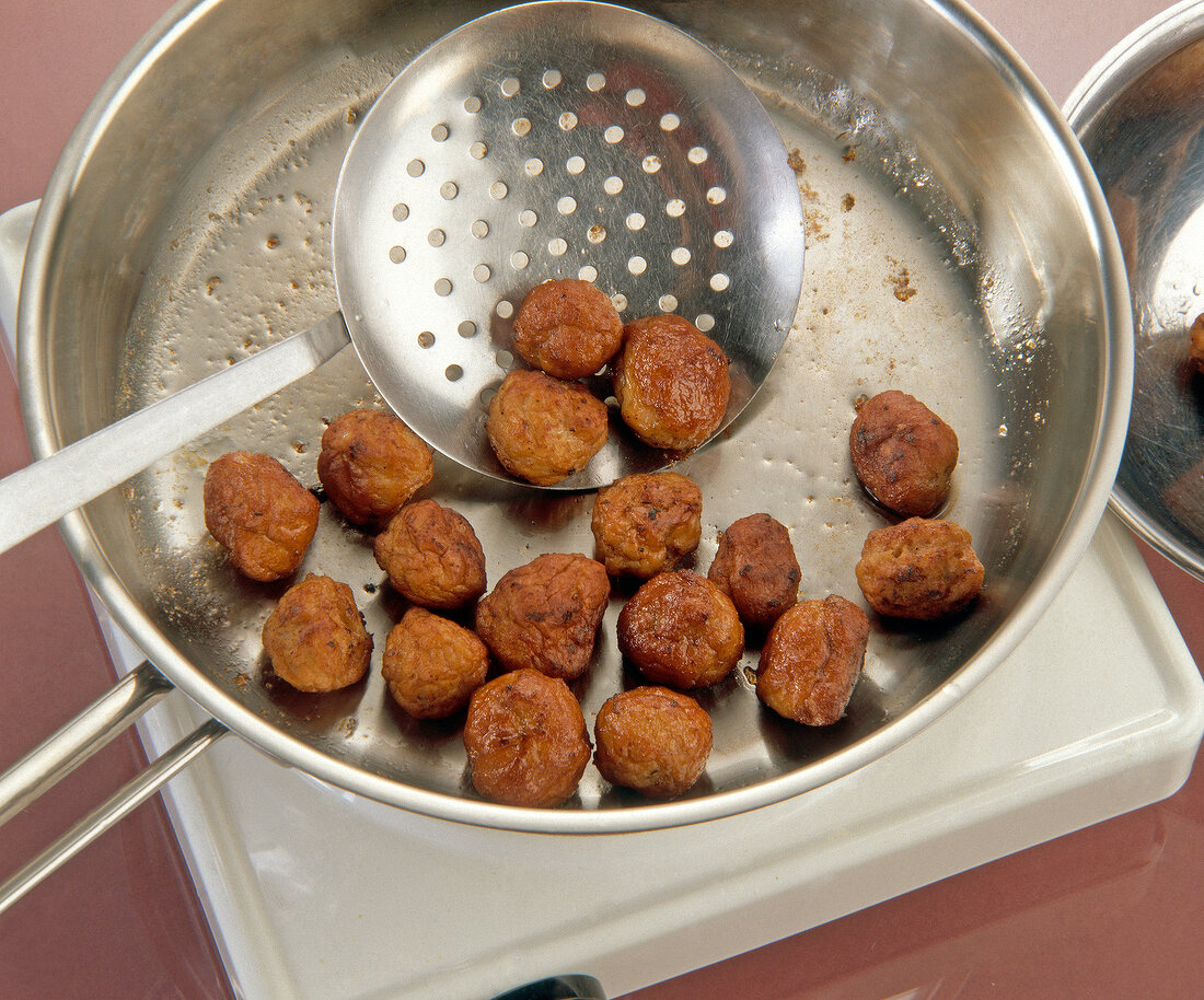 Fried dumplings with frying spoon in steel pan on white board