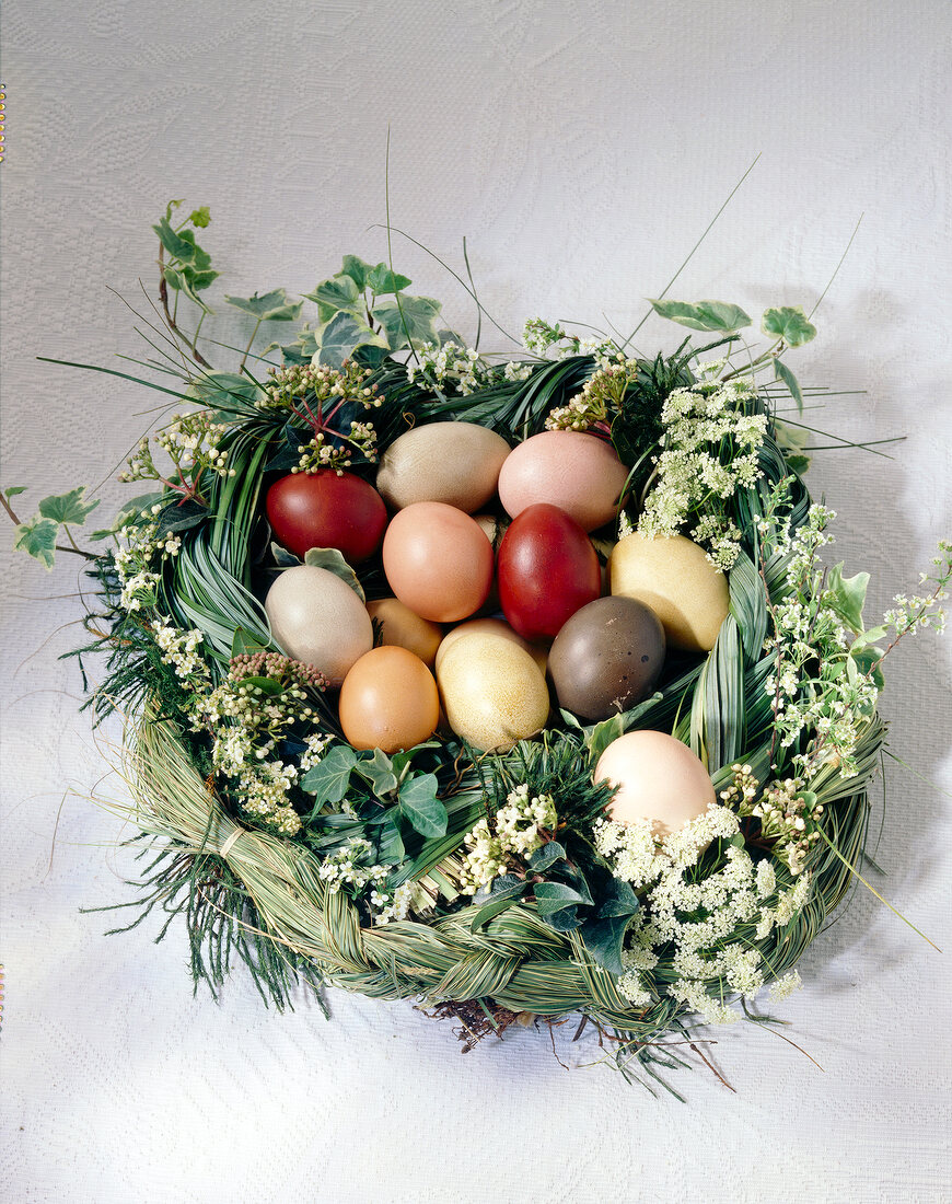 Gebundenes, geflochtenes Nest aus Gräsern und Blüten mit bunten Eiern