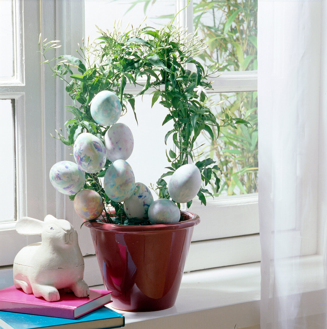 Blütenkranz mit bunten Eiern in einem Blumentopf auf Fensterbank