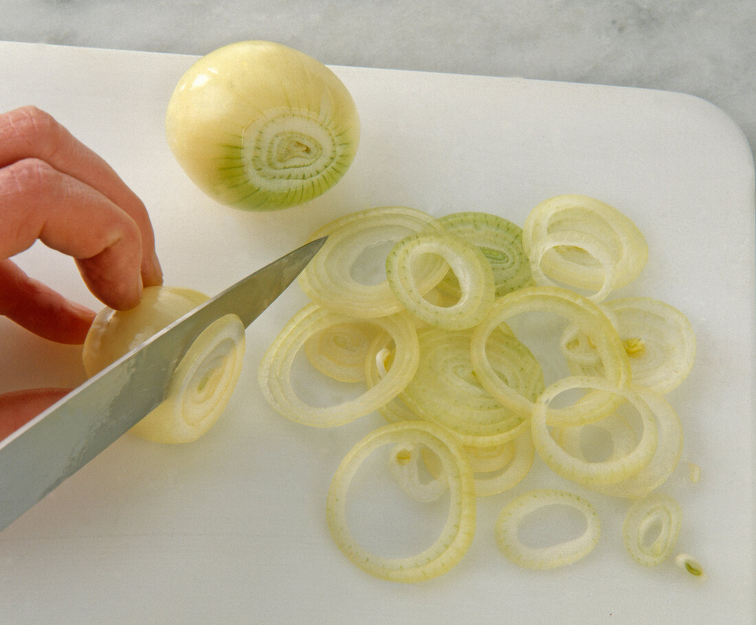 Green onions cut in rings with knife on white chopping board