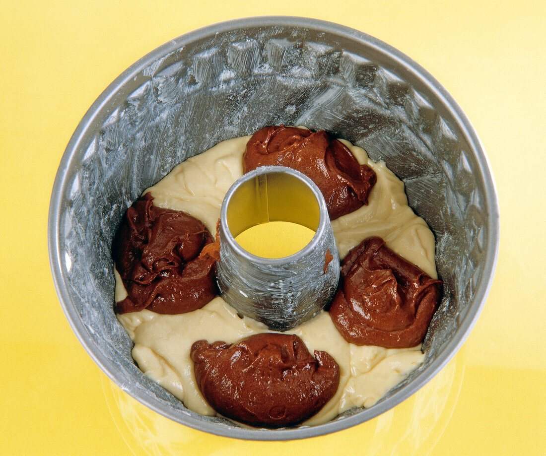 Gugelhupf with light and dark batter filled in bowl on yellow background