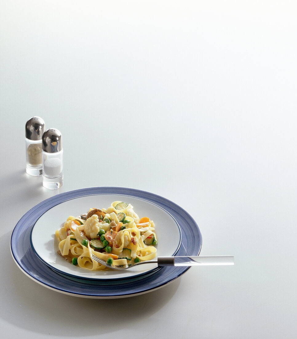 Vegetable pasta on plate beside salt and pepper shakers on white background