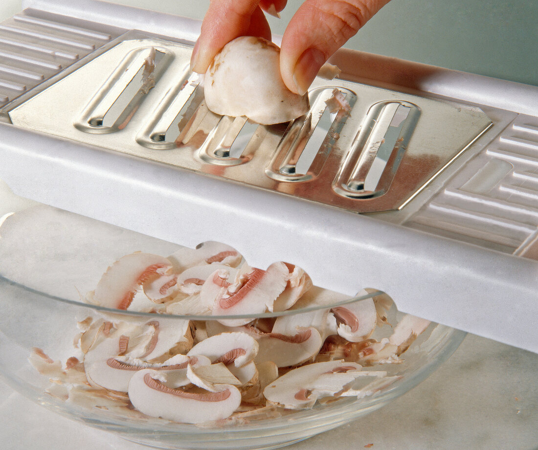 Close-up of mushrooms being sliced into thin slices with a vegetable slicer