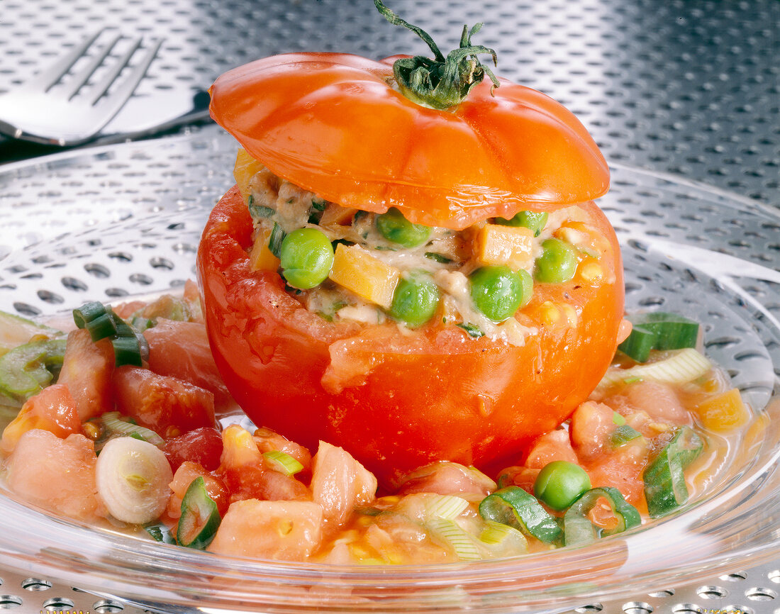 Close-up of stuffed tomato with sausage, peas, carrots and onions on glass plate
