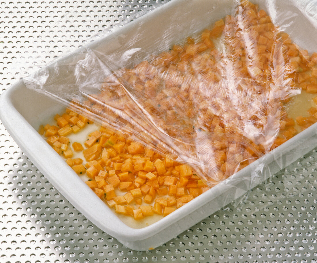 Close-up of diced carrots in ovenproof dish covered with plastic foil