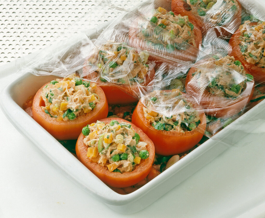 Close-up of stuffed tomatoes in baking dish covered with plastic foil
