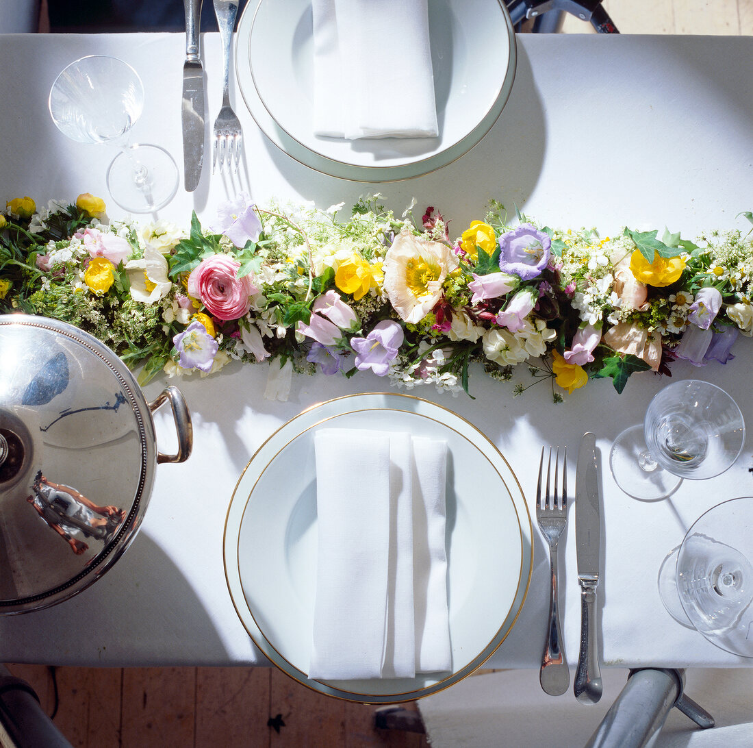Garland of flowers on white table cloth between place settings, elevated view
